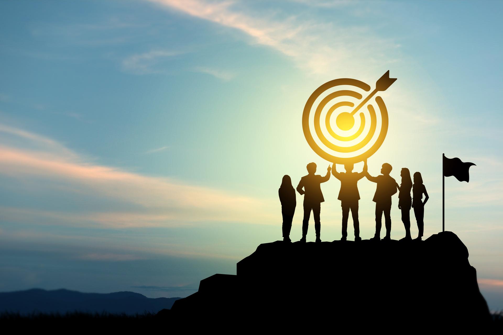 Goal setting towards planning for the future. Silhouettes of group businessmen holding target boards with flags planted on a mountain.