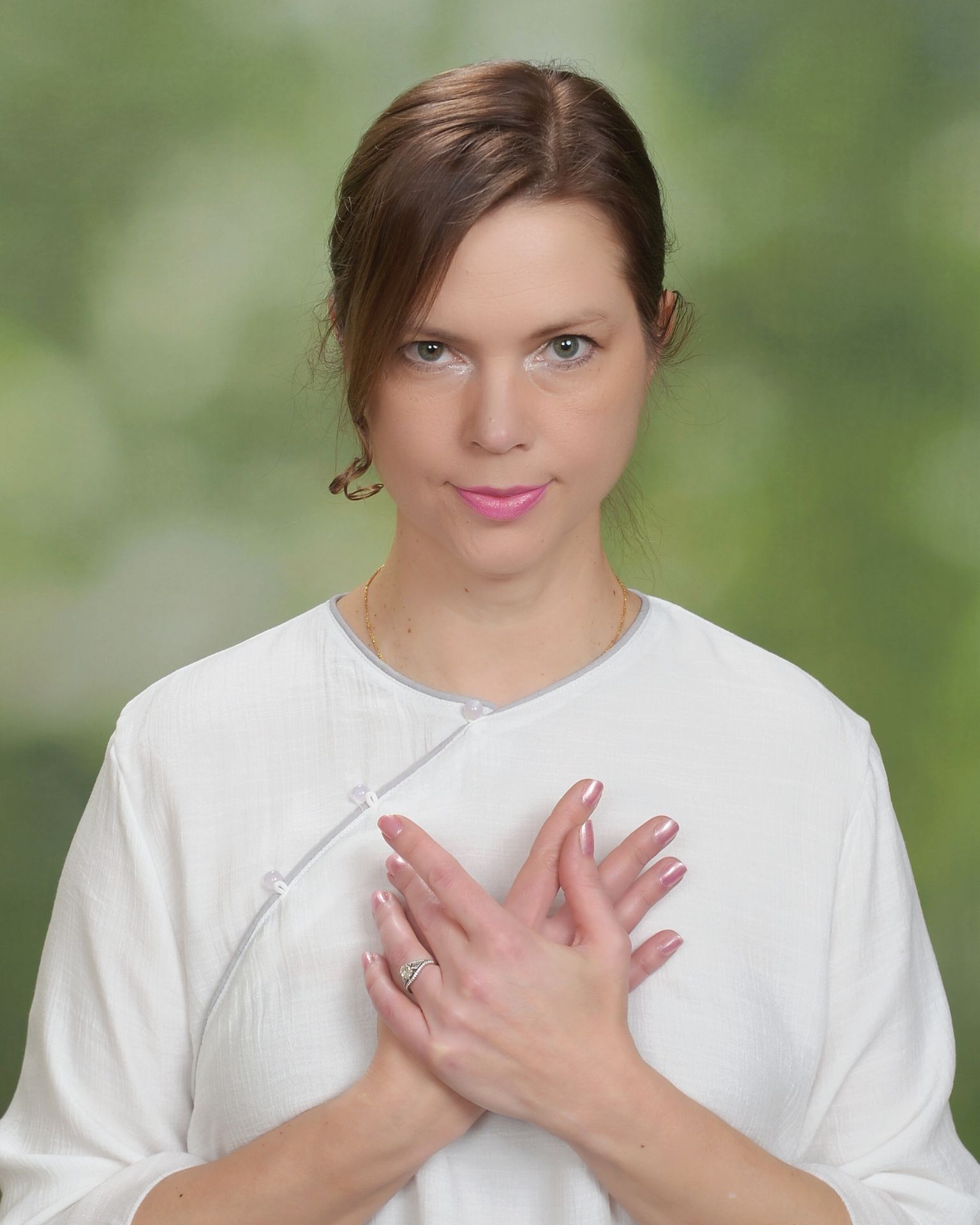 Person in white shirt with hands crossed over chest, against a blurred green background.