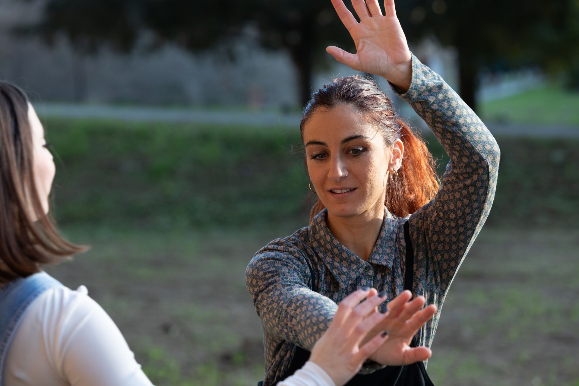 Two young women performing tai chi chuan exercises in a public park