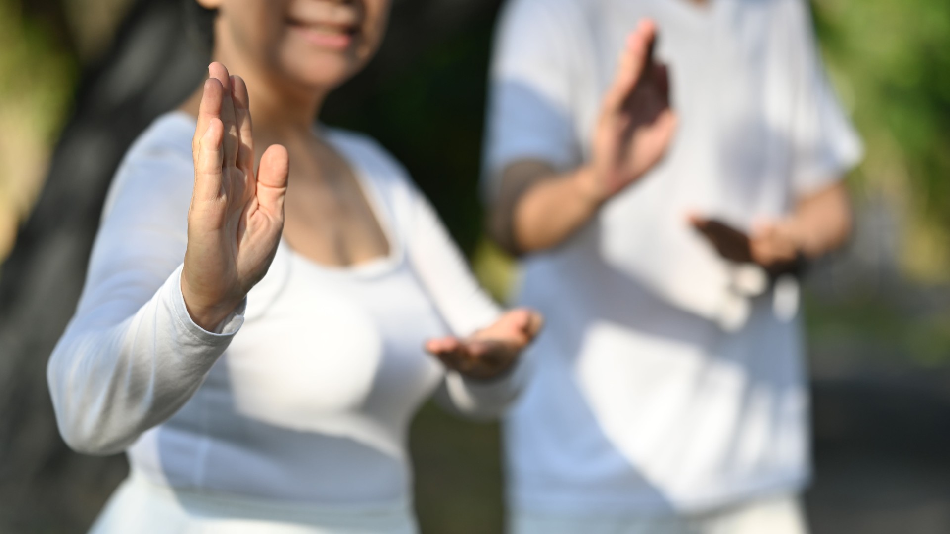Active middle age couple in white clothing working out with Tai Chi in the park. Health care and wellbeing concept.